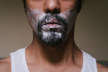 Primer plano de parte del rostro de un hombre latino que tiene espuma en la barba y usa ropa...
