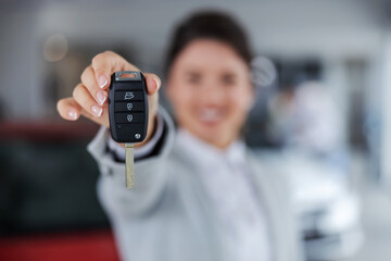 Closeup of car seller holding and handing a car keys towards camera while standing in car salon.