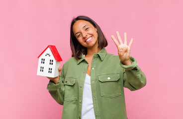 young hispanic woman smiling and looking friendly, showing number four or fourth with hand forward,...