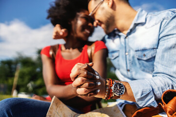 Obraz premium Closeup of young smiling multicultural hipster couple holding hands and sitting outdoors on a beautiful sunny day.