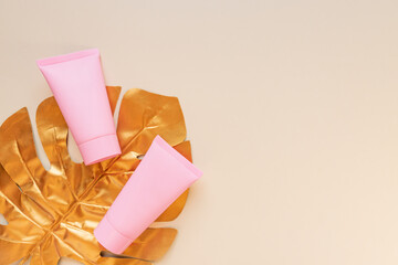 Top view of a pink tube of cream mockup with a golden monstera leaf on a pink background. Unbranded cosmetics package.