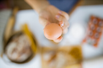 Obraz na płótnie Canvas Female hand holding an egg above ingredients on a table