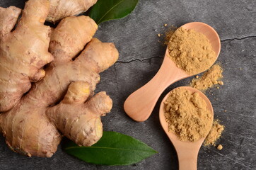 Fresh ginger root on a black stone background and ginger powder in the wooden spoon. Copy space,...