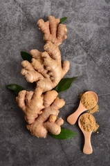Fresh ginger root on a black stone background and ginger powder in the wooden spoon. Copy space, top view