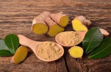 Fresh ginger root and ginger powder in the wooden spoon on a old wooden background. Green leaves