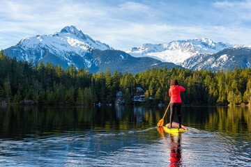 Adventurous Girl Paddle Boarding on Levette Lake with famous Tantalus Mountain Range in the background. Taken in Squamish, North of Vancouver, British Columbia, Canada.