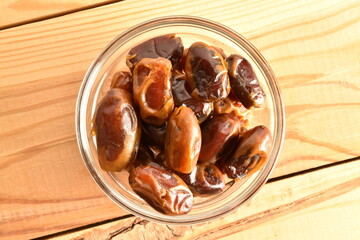 Several natural dried dates in a ceramic bowl, close-up, on a wooden table.