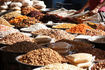 Assorted nuts and dried fruits on market counter. Metal bowls with various cereals at food market. Healthy vegan food.