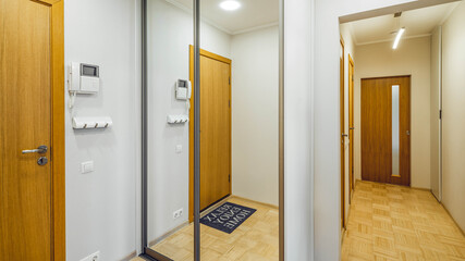 Contemporary interior of entrance hall in flat. Wooden doors. Wardrobe with mirror. Narrow hallway.