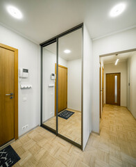 Modern interior of entrance hall in luxury apartment. Wooden door. Sliding door wardrobe with mirror. Narrow hallway.