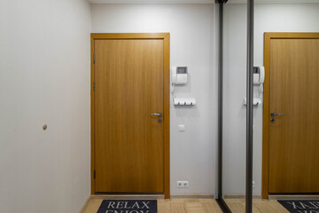 Modern interior of entrance hall in apartment. Front view of wooden door. White wall. Mirror sliding door wardrobe.