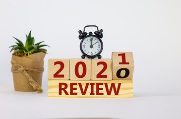 Naklejka premium Review 2021 symbol. Fliped wooden cube and changed words 'Review 2020' to 'Review 2021'. Black alarm clock and house plant. Beautiful white background, copy space. Business and 2021 new year concept.