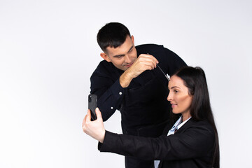 A male make-up artist do makeup of a young businesswoman who takes a selfie on smartphone. Gender stereotypes on white.