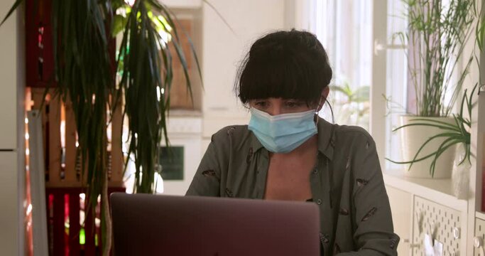 Brunette woman video calling through computer with mask at home