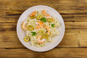 Spaghetti pasta with prawns, green olives and parsley on wooden table. Top view