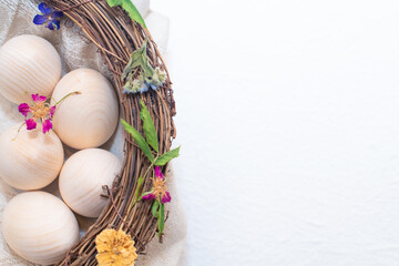 Unpainted wooden Easter eggs in the nest and decorated with flowers and leaves on white background. Set of Easter eggs for kids colouring and DIY crafting. Easter holidays concept with copy space.