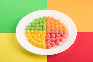 Gummy candy, arrangement of gummy candy arranged by color on a white plate on a colored surface.