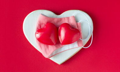 Red hearts with a protective pink mask on a wooden heart on a red background. Valentine's day concept care.