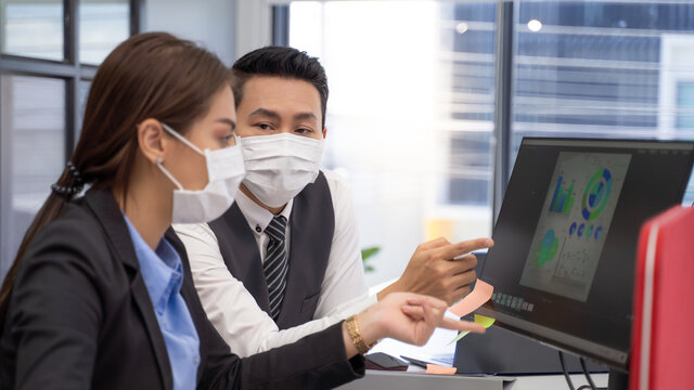 
Two analysts with face masks discussing financial data on computer.