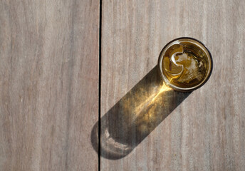 A cup of beer and ice on wooden table with sunlight and shadow.