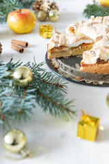 gedeckter Kuchen mit Apfel und Marzipan mit einer Haube aus Baiser auf einem Tisch aus Holz zur Weihnachtszeit mit Zweigen von der Tanne oder einem Nadelbaum