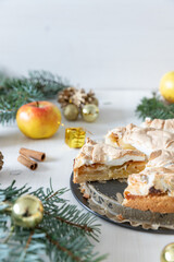 gedeckter Kuchen mit Apfel und Marzipan mit einer Haube aus Baiser auf einem Tisch aus Holz zur Weihnachtszeit mit Zweigen von der Tanne oder einem Nadelbaum