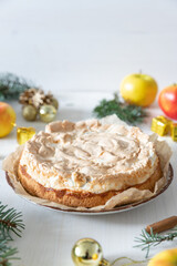 gedeckter Kuchen mit Apfel und Marzipan mit einer Haube aus Baiser auf einem Tisch aus Holz zur Weihnachtszeit mit Zweigen von der Tanne oder einem Nadelbaum