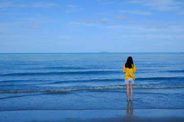 Back side of a girl in yellow shirt standing in the sea looking at the horizon.