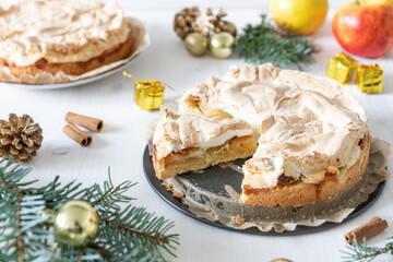 gedeckter Kuchen mit Apfel und Marzipan mit einer Haube aus Baiser auf einem Tisch aus Holz zur Weihnachtszeit mit Zweigen von der Tanne oder einem Nadelbaum