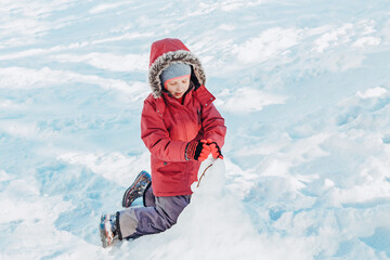 Fototapeta na wymiar Funny happy girl child in warm clothes playing with snow in park outside. Child kid making snowman during cold winter sunny bright day. Kids outdoors seasonal activity.