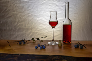 Leckerer Schlehenlikör in einem Schonen Glas und Flasche auf einem Holzbrett mit Schlehen im...