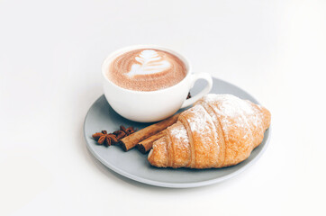 Fresh baked croissant with coffee cup and latte art, cinnamon and star anise.Isolated
