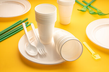 Disposable plastic dishware waste. Group of empty plates, cups, forks and utensils on yellow table