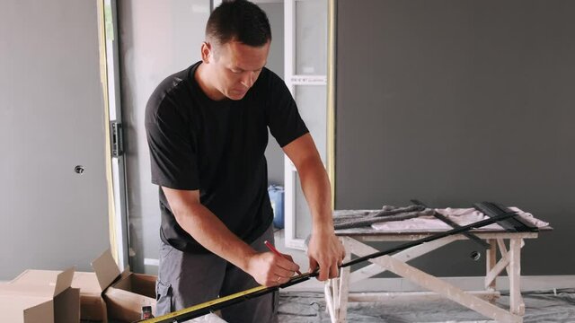 Professional worker installing ceiling. The man is marking a metal profile to cut it.