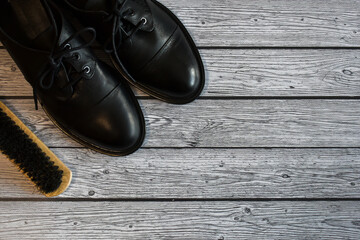 Black leather shoes and brush for cleaning shoes on a gray wooden background. A pair of stylish women's boots on the laminate floor, top view. Concept: Leather shoe care, shoe repair. space for text