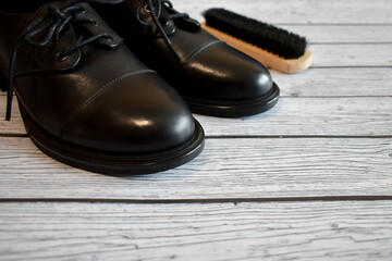 Black leather shoes and brush for cleaning shoes on a gray wooden background. A pair of stylish women's boots on the laminate floor, top view. Concept: Leather shoe care, shoe repair. space for text