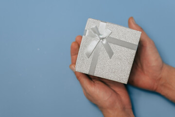Male hands holding a gift or real box are decorated with confetti stars on a blue table