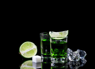 Absinthe shots with lime slices and sugar on black background