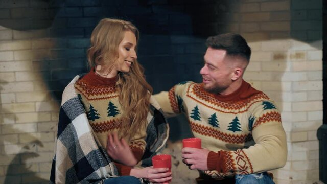 Loving couple is warming in the evening near fireplace. Same knitted sweaters on male and female. Love story concept.