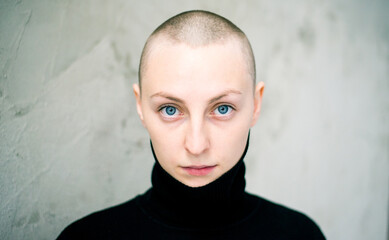 young caucasian woman with shaved hair on her head, almost bald, looks at the camera
