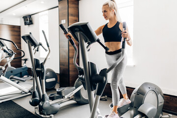 sportive young woman, in sportswear, trains on a cardiovascular machine in the gym