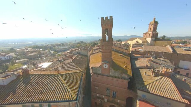 Drone Flying Over Tiled Roof Buildings Towards Palazzo Pretorio With Church Of San Martino In Background In Sinalunga, Siena, Italy. - FPV, Aerial