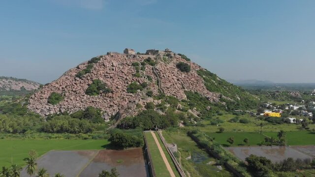 Green and lush landscape surrounding the rocky mountain that is home to Krishnagiri Fort in India.