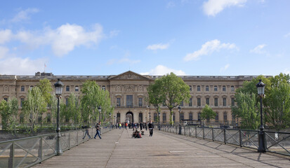 View of the Louvre Palace from the Bridge of Arts. On the bridge walk people, photographers are prepared to shootin