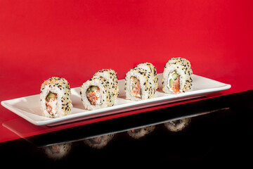 Obraz na płótnie Canvas Sushi Sets Nigiri, Uramaki, California, Philadelphia, on a white plate. On a red colored background.