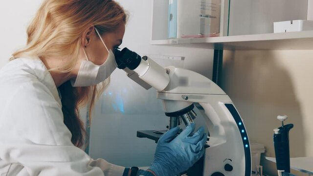 Scientist microbiologist examines biological blood samples under a microscope. Female researcher conducts research under a microscope in a laboratory