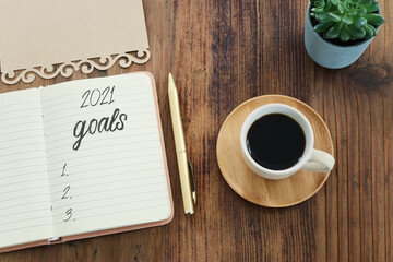 Business concept of top view 2021 goals list with notebook, cup of coffee over wooden desk