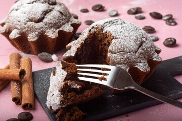Chocolate cupcake sprinkled with powdered sugar on a pink background. Sweet chocolate pastries. Sweets. Chocolate cupcake broken off piece