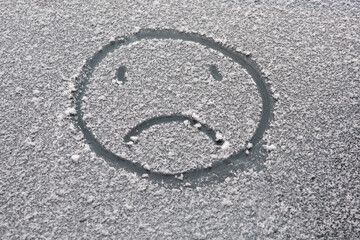 sad face painted on the snow-covered car window
