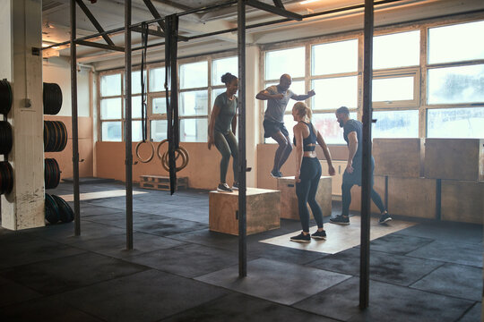 Diverse people doing box jumps together in a gym
